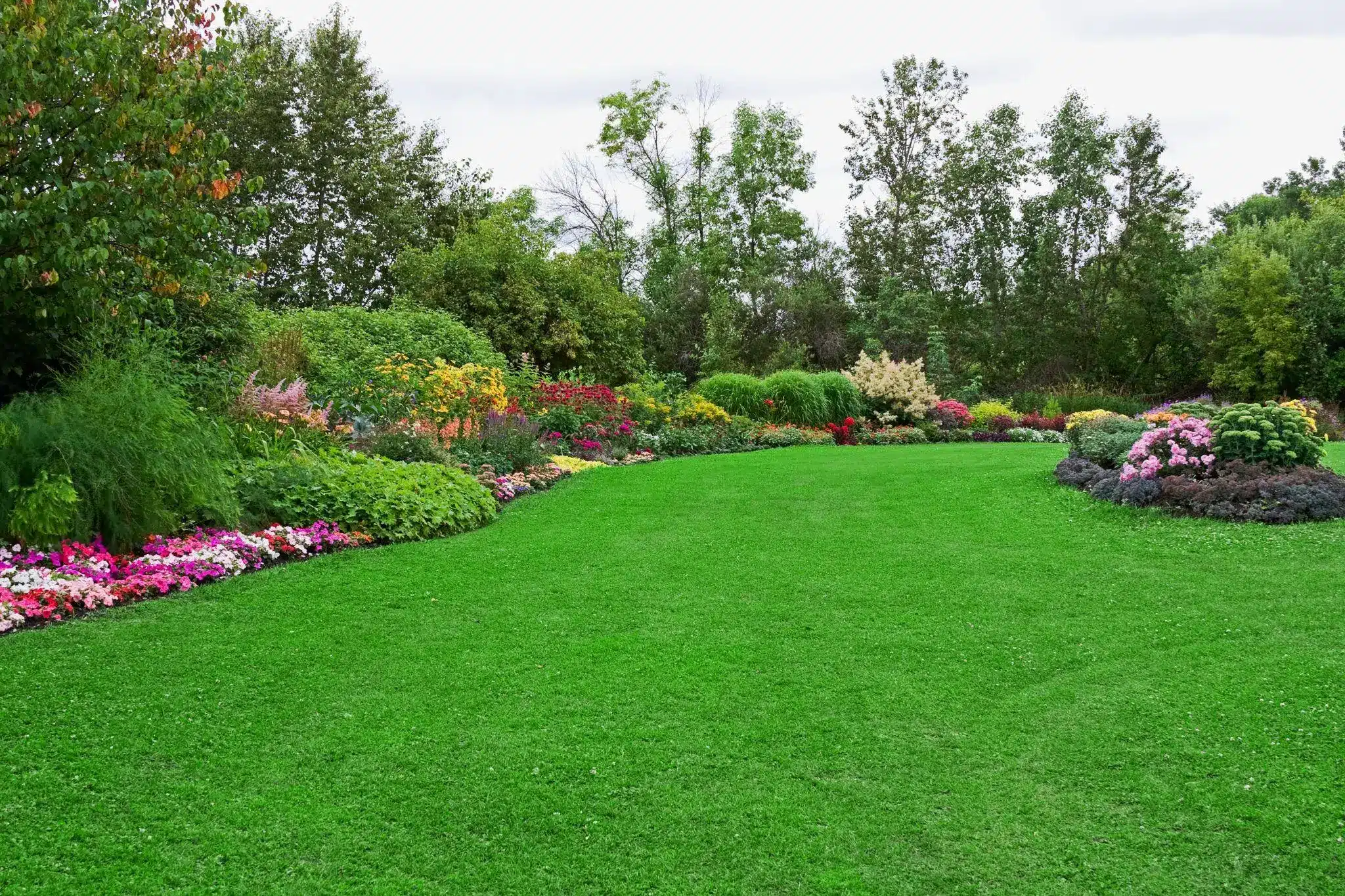 Lush garden landscape with colorful flower beds and vibrant green grass under cloudy sky