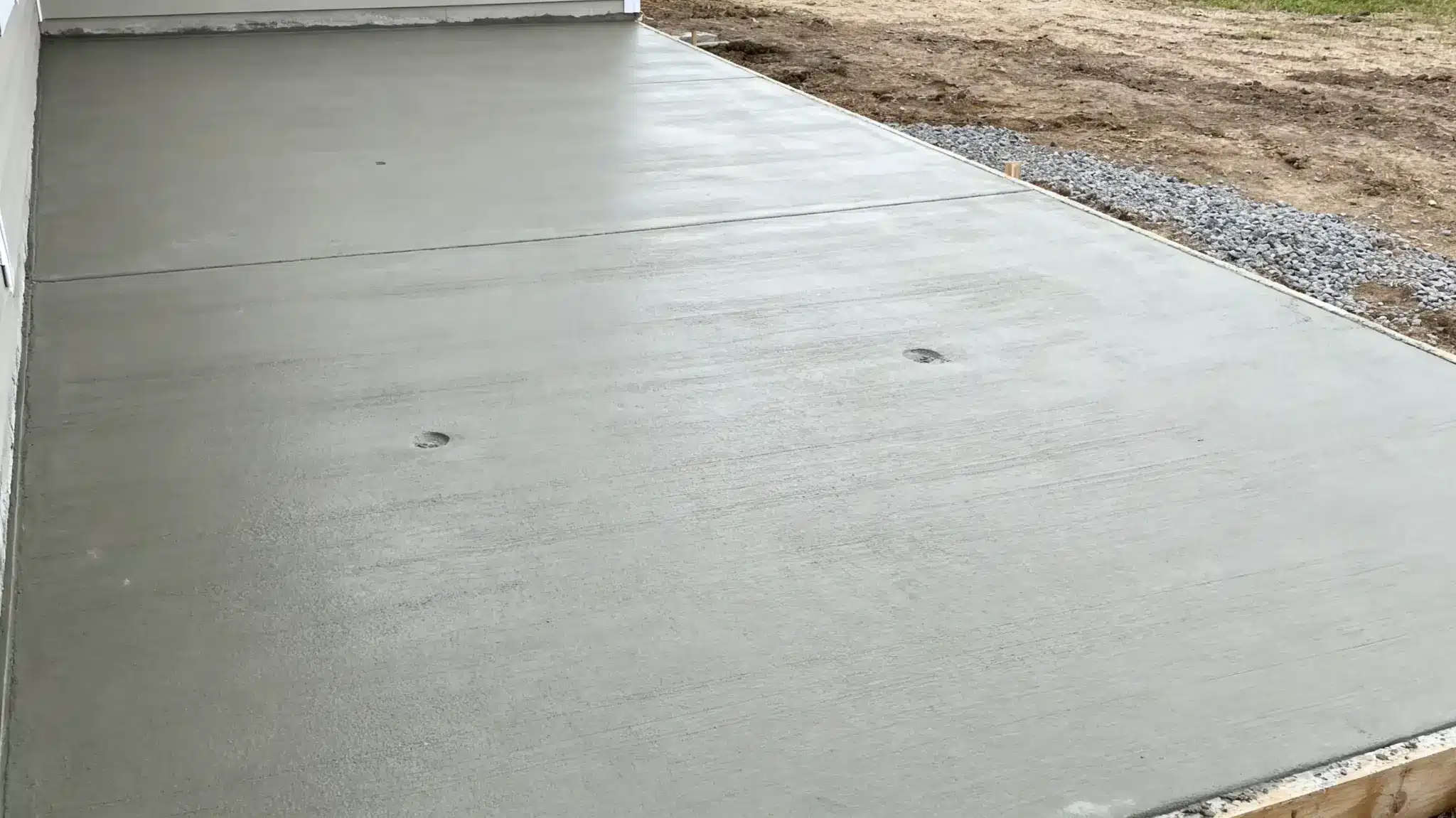 Newly poured concrete patio drying in outdoor setting with gravel border