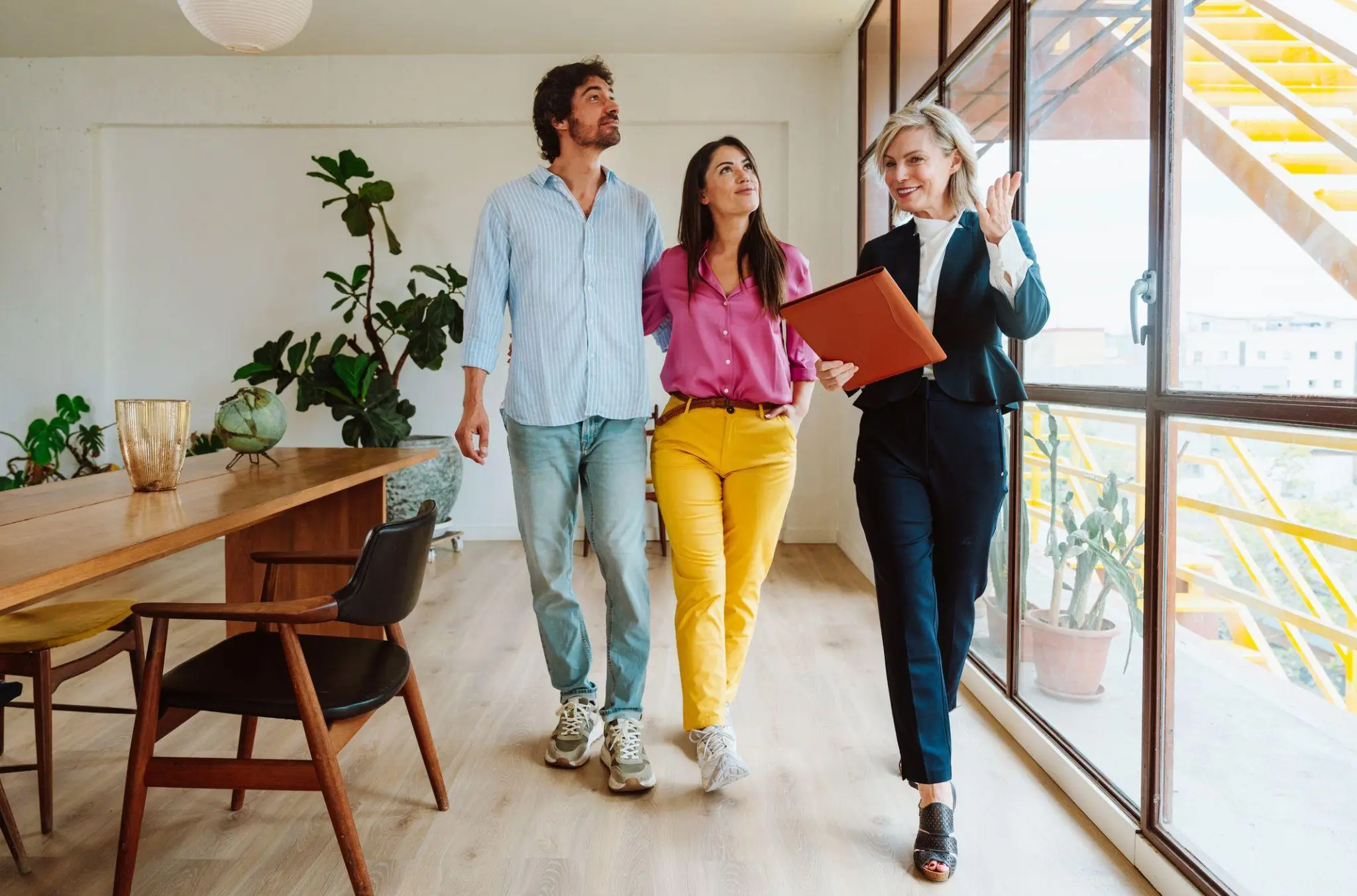 Real estate agent showing couple a bright living room with large windows and wooden floor