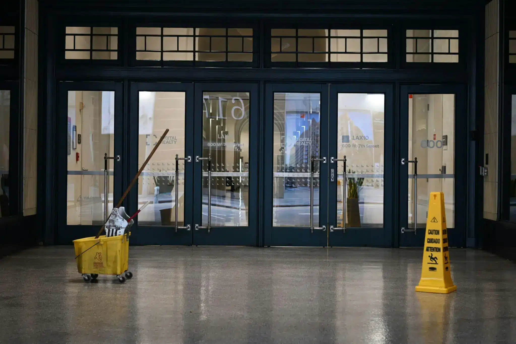 Yellow mop bucket and caution sign in empty lobby with glass doors
