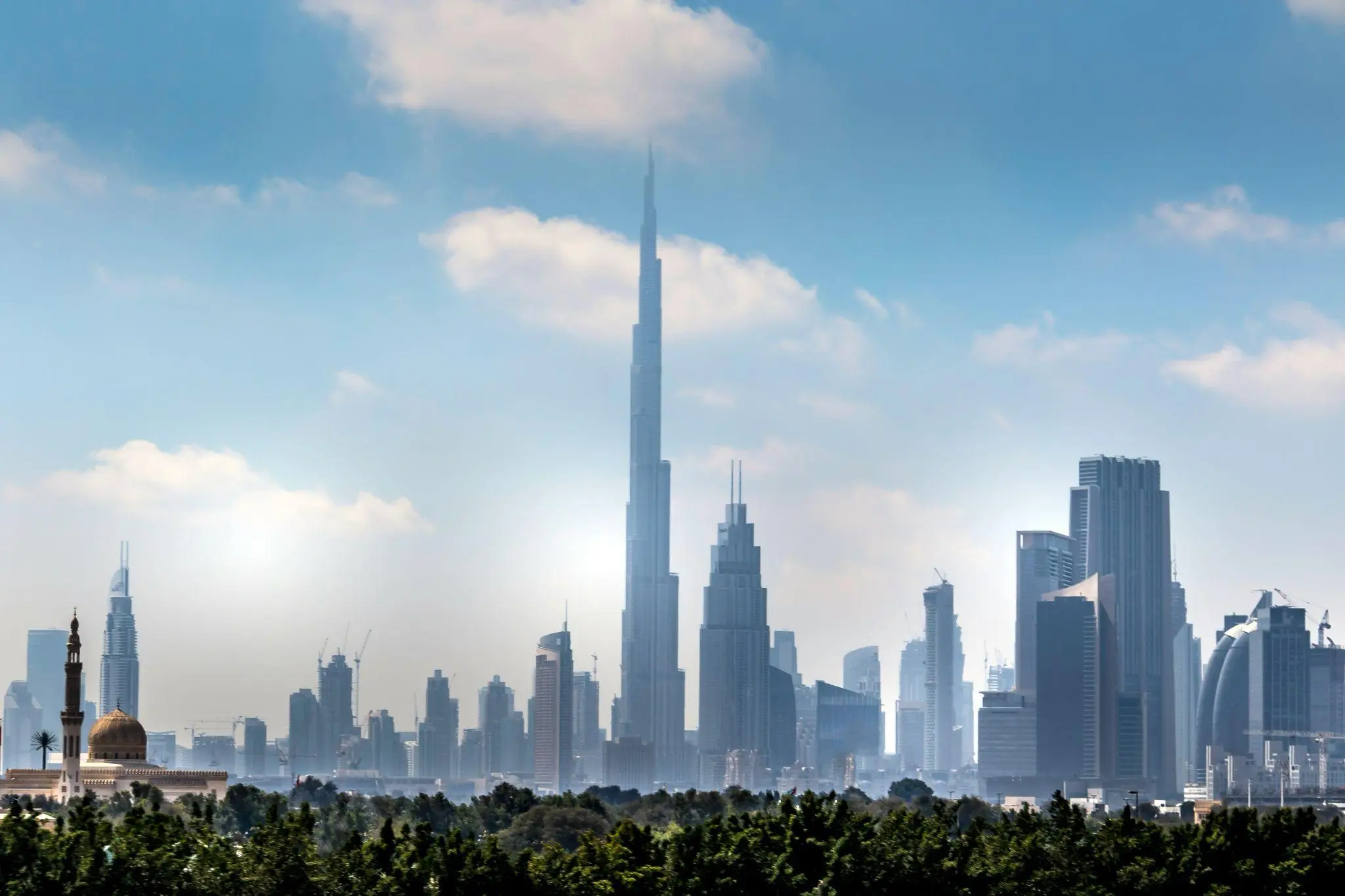 Skyline with tall skyscraper under blue sky and scattered clouds, trees in foreground