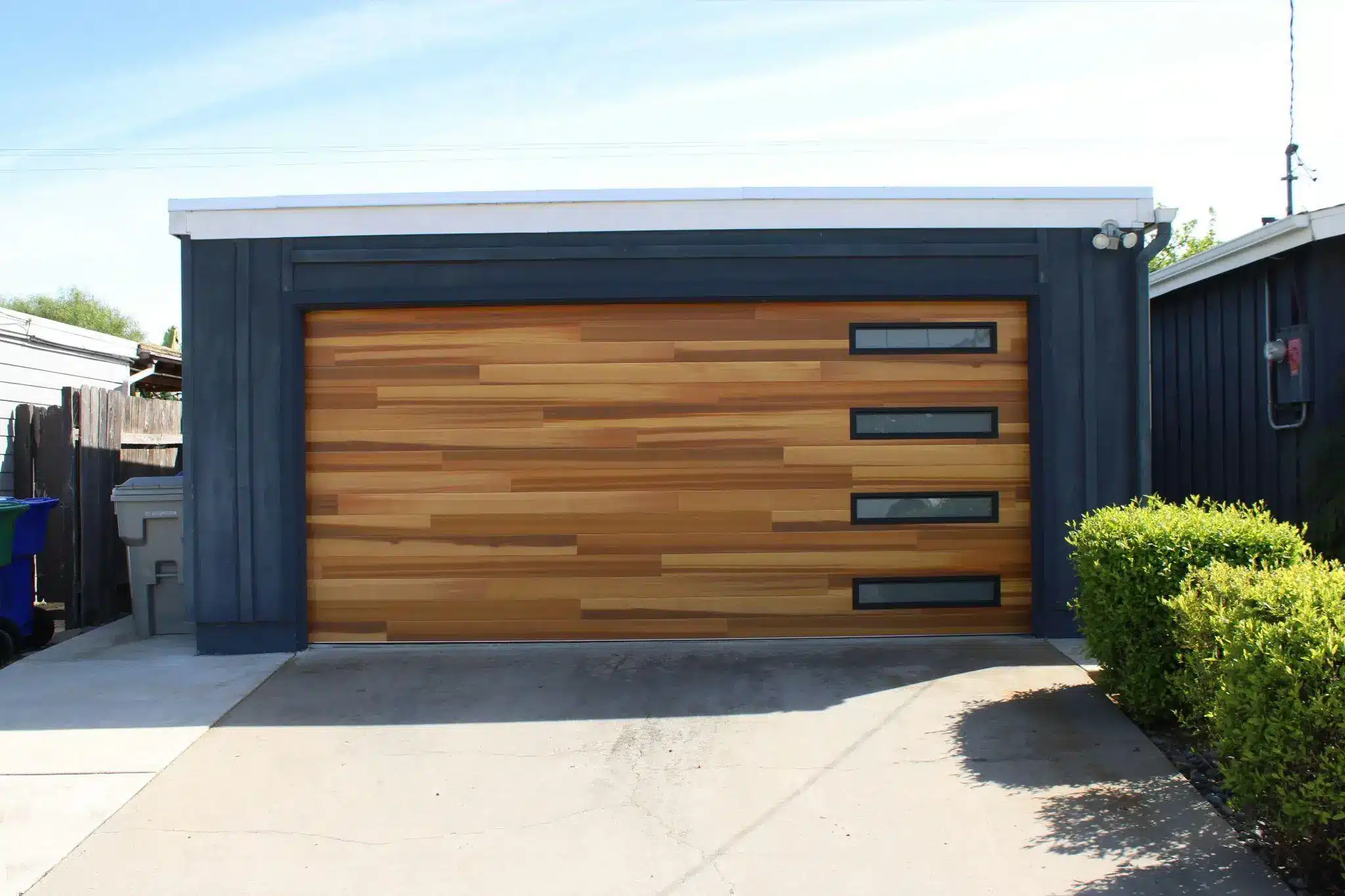 Wooden garage door with rectangular windows in modern driveway surrounded by greenery