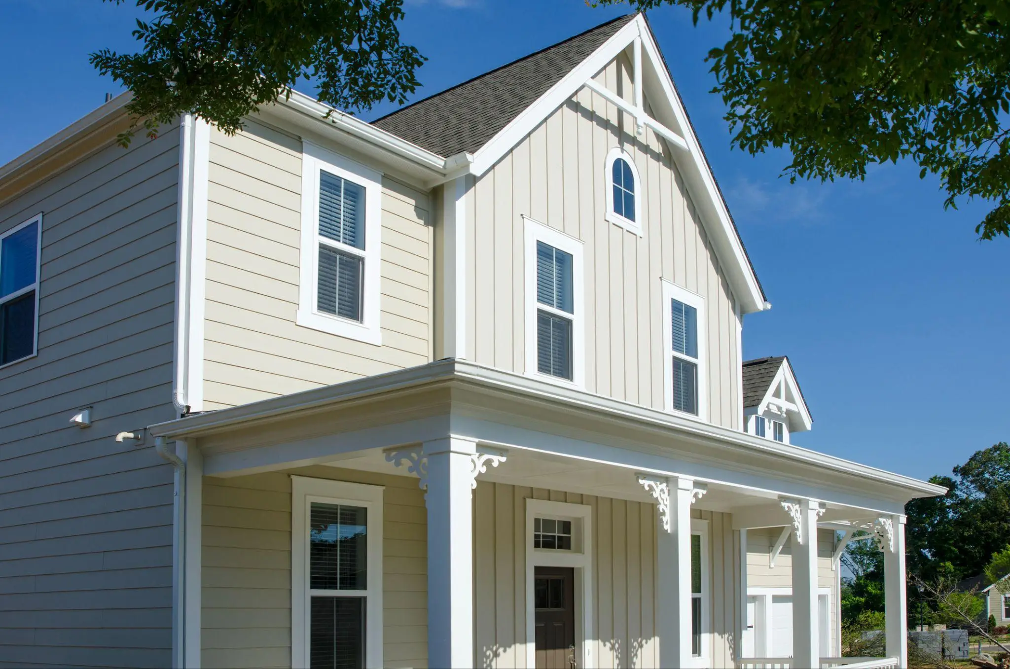 Victorian-style beige house with gabled roof and decorative trim under clear blue sky