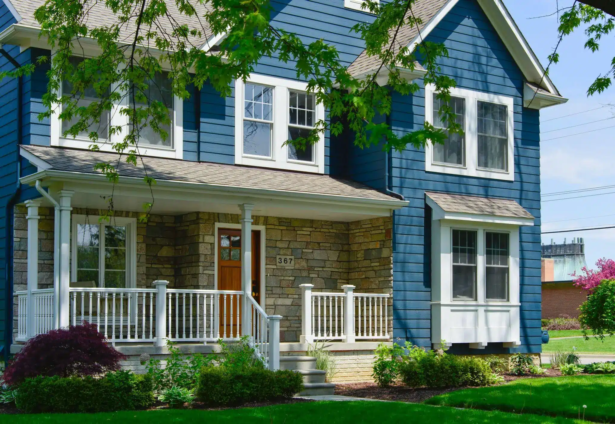 Blue house with stone facade and porch, surrounded by green lawn and trees