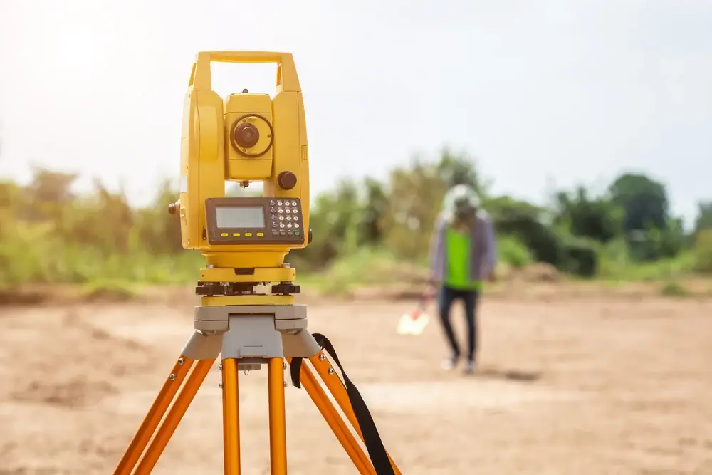 Yellow theodolite on a tripod with a surveyor in the blurred background outdoors
