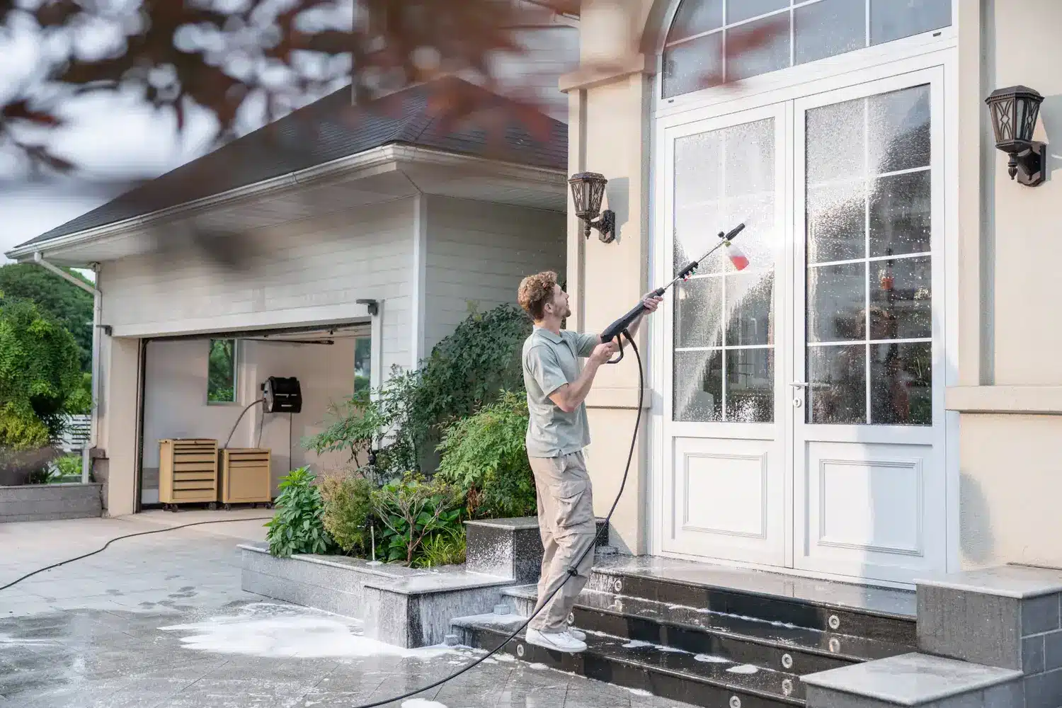 Man using pressure washer to clean glass doors of house exterior steps