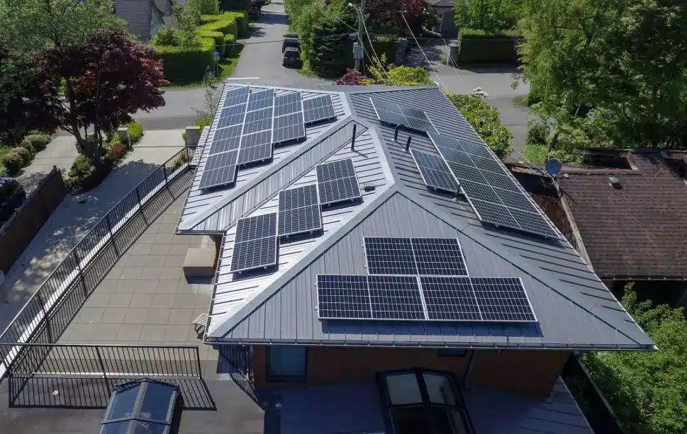 Rooftop solar panels on modern house surrounded by trees and driveway in suburban neighborhood