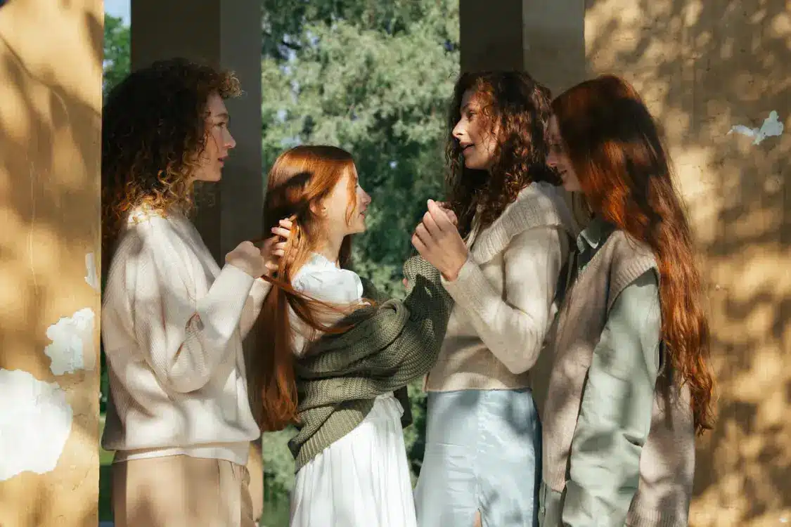 Four women with long hair conversing outdoors in dappled sunlight