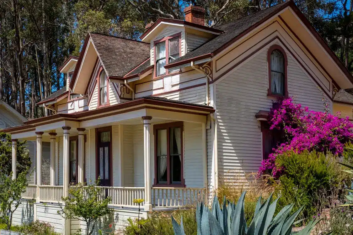 Victorian-style house with brown trim and blooming bougainvillea in a lush garden setting