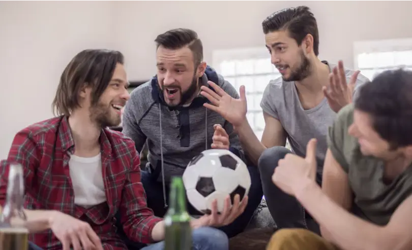 Group of four men excitedly watching a soccer game indoors holding soccer ball