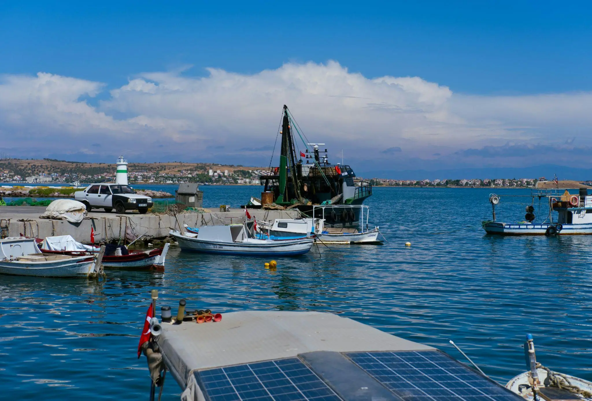 Fishing boats docked in a sunny harbor with distant lighthouse and small town view