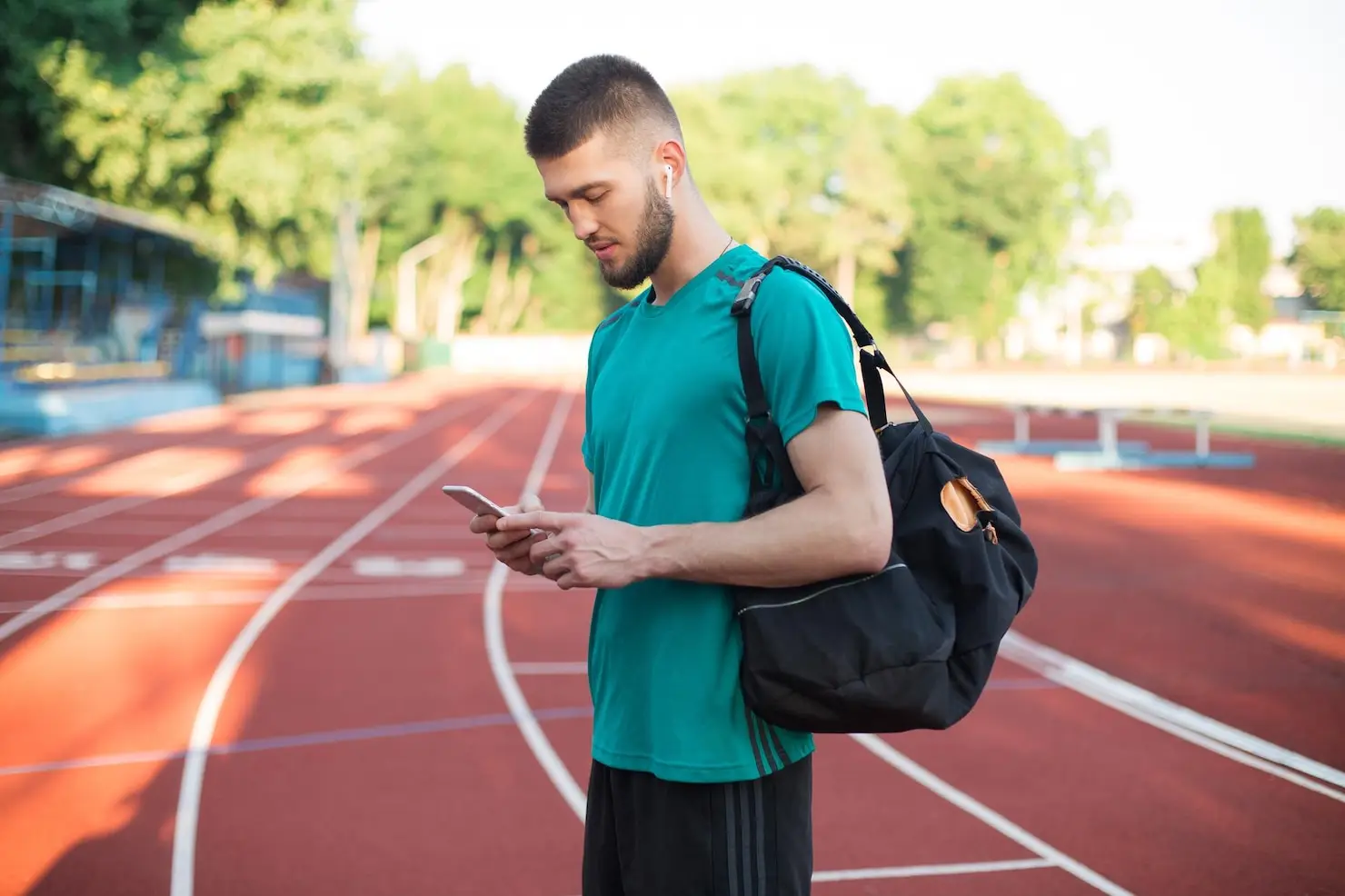 Man in green shirt listening to music on phone at outdoor running track