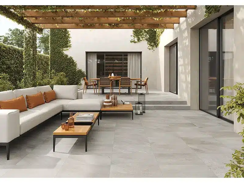 Outdoor patio with modern furniture under pergola, featuring beige sectional sofa and wooden dining table