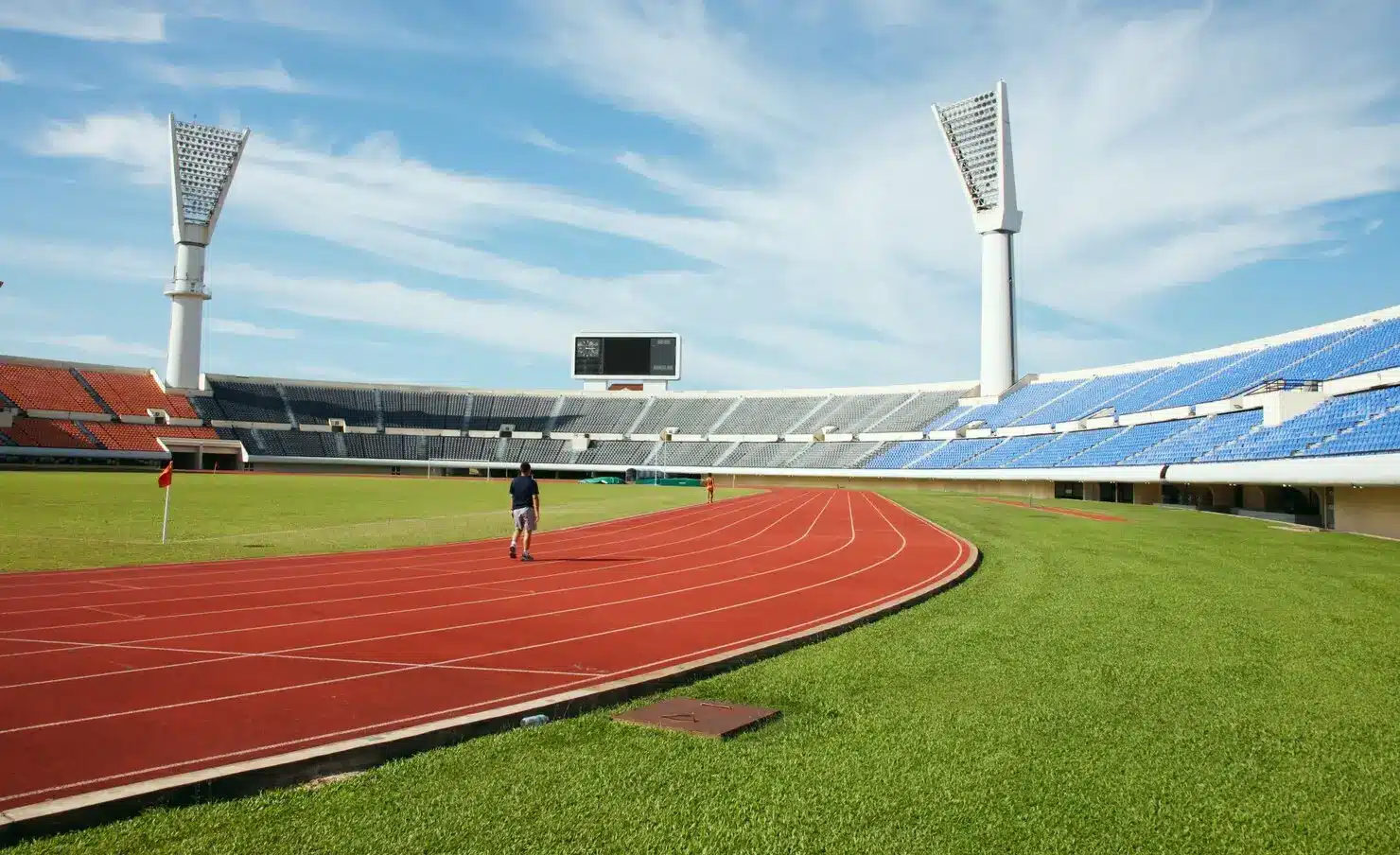 Man walking on red athletics track in large outdoor stadium with empty seats