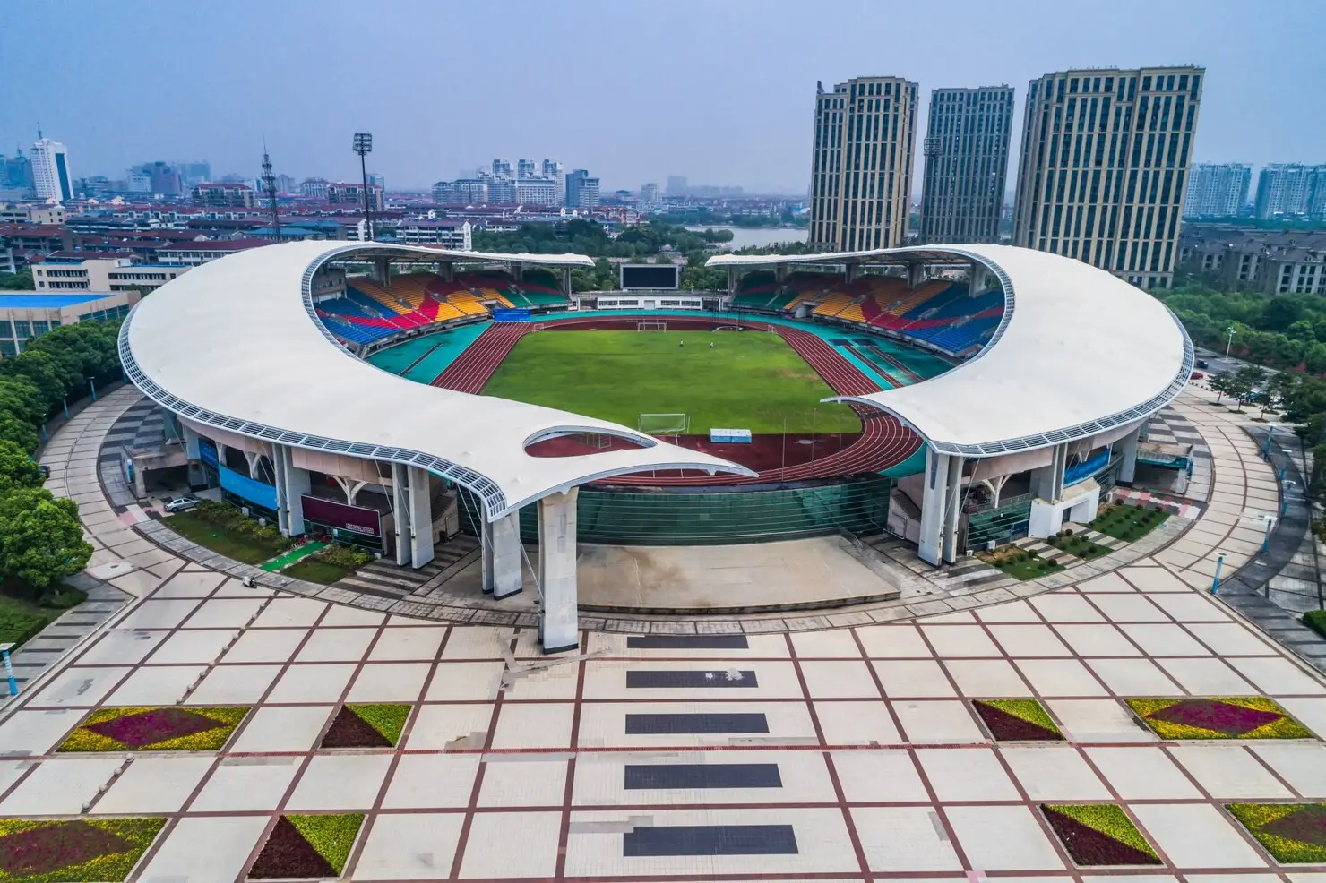 Large outdoor stadium with colorful seating and track surrounded by urban landscape