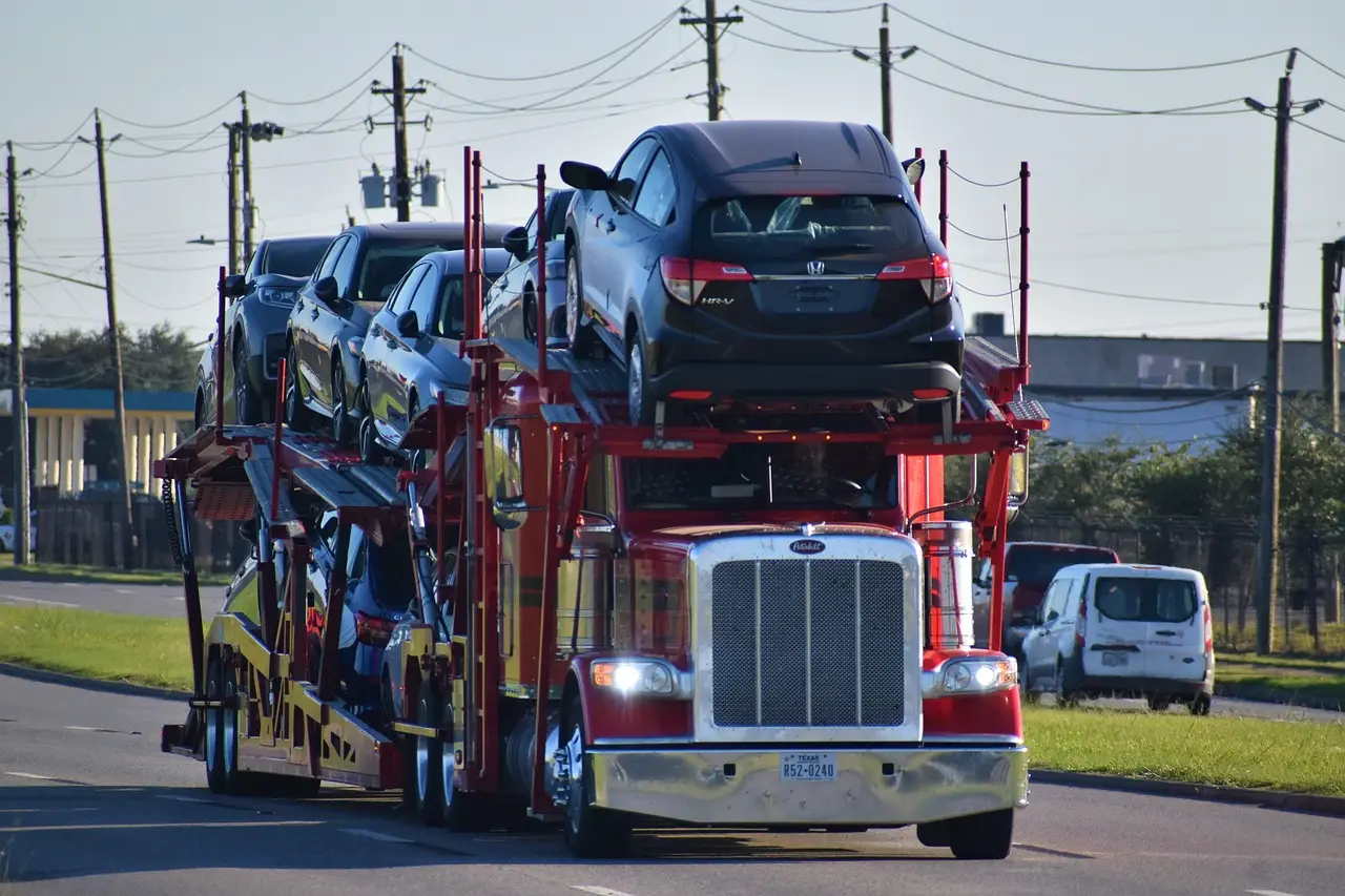 Red semi-trailer carrying multiple cars on a highway under clear sky