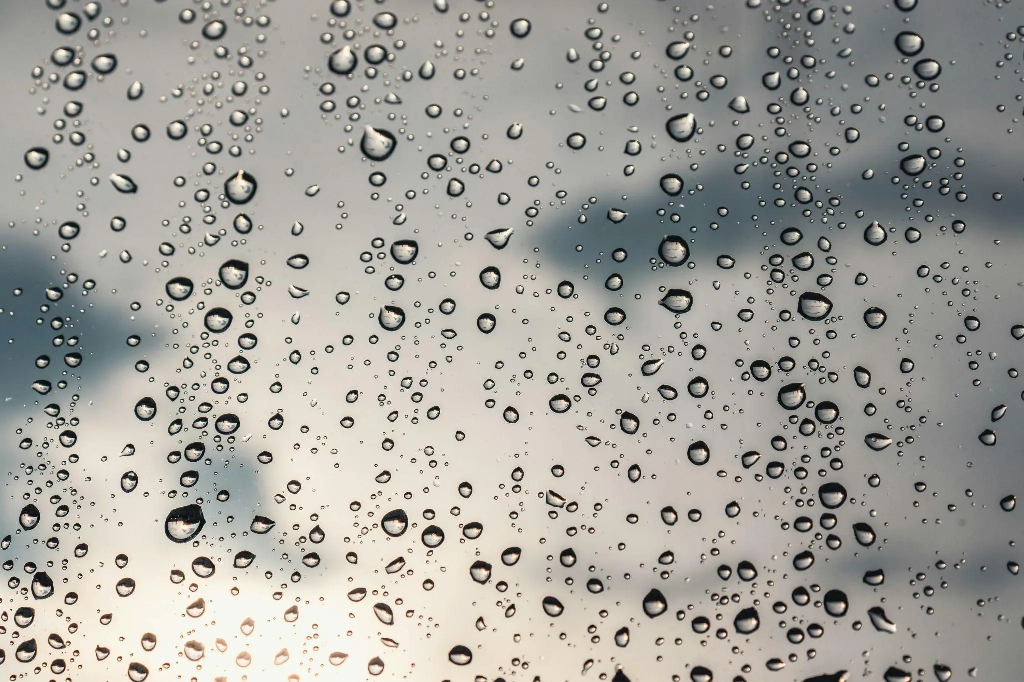 Raindrops on a glass window with cloudy sky in the background