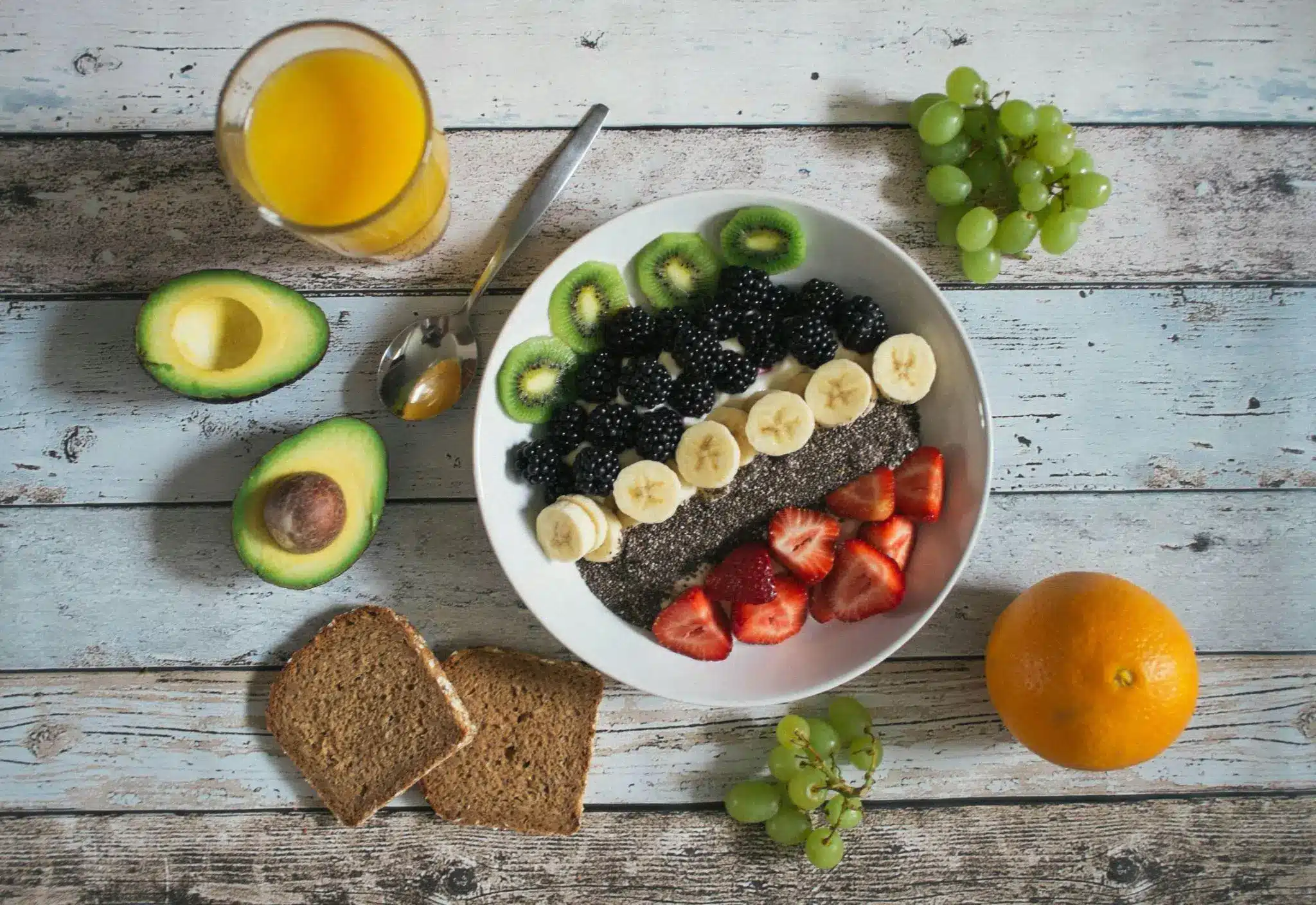Bowl of chia pudding with fruit slices on rustic wooden table with avocado and orange juice
