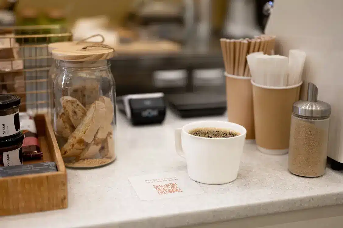 Coffee cup on cafe counter with biscotti jar and disposable cups