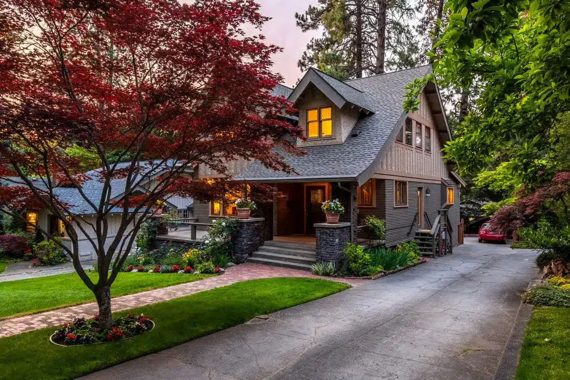 Craftsman-style house with illuminated windows and lush garden at dusk