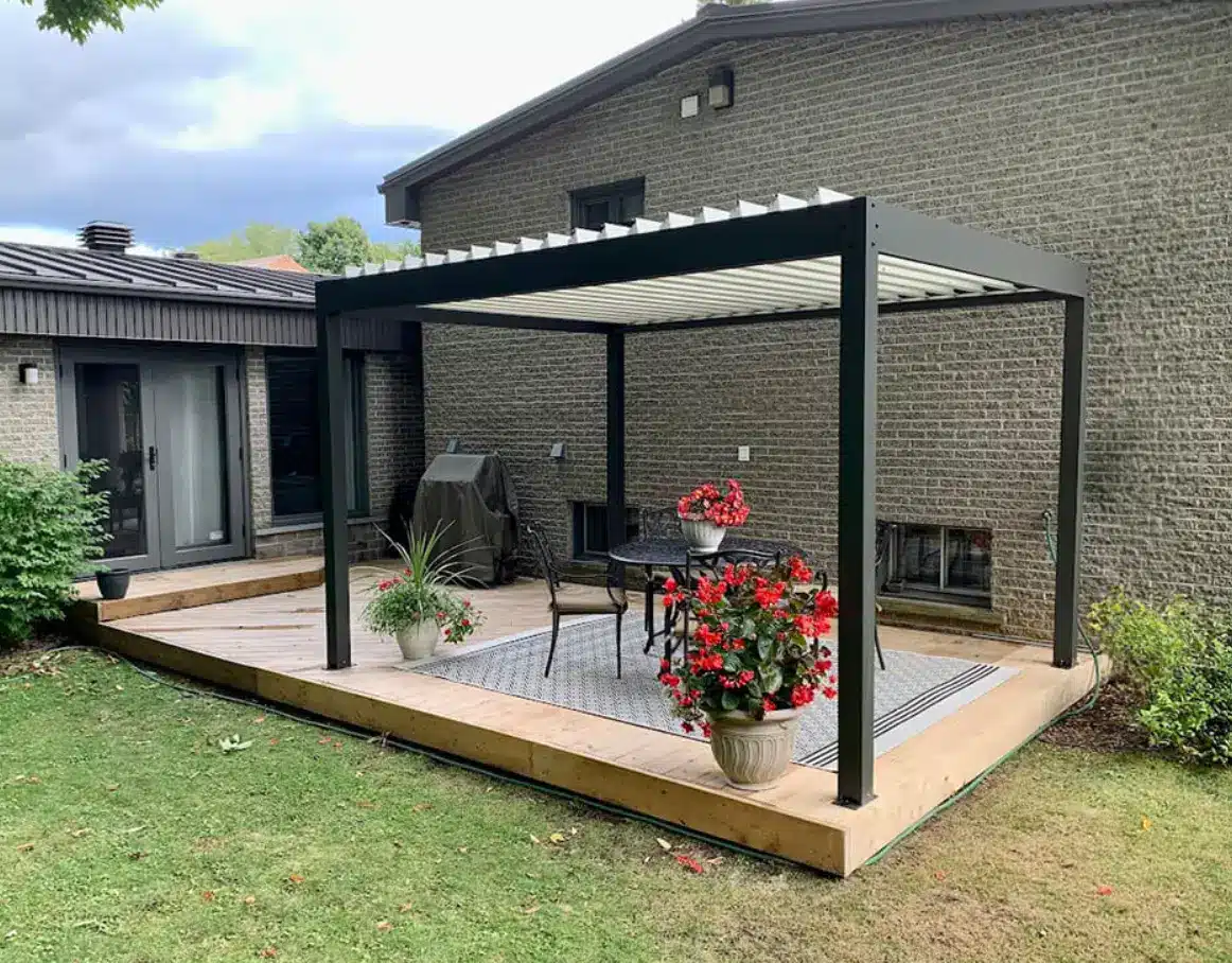 Outdoor pergola with metal frame and potted plants on wooden deck beside brick house