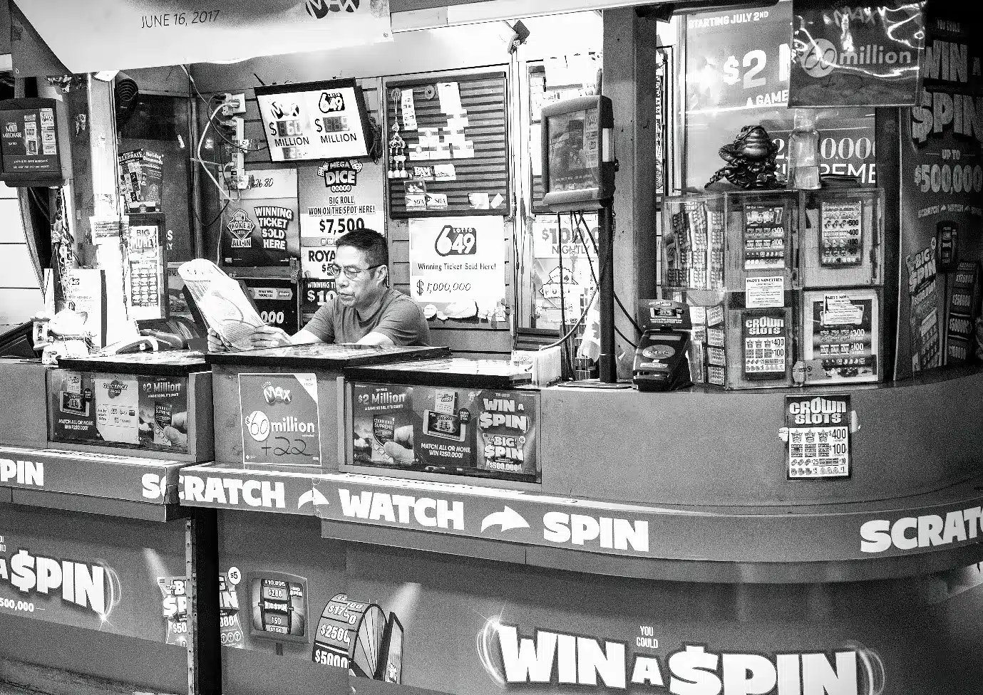 Man reading a newspaper at a busy lottery ticket booth with various posters and advertisements