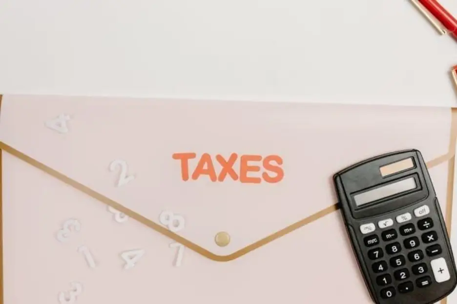 Calculator on pink envelope labeled "TAXES" with scattered numbers nearby