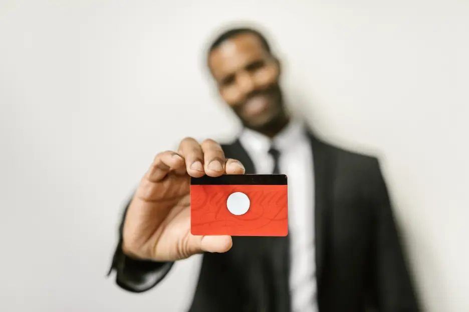 Man in suit holding a red credit card towards the camera in an office setting