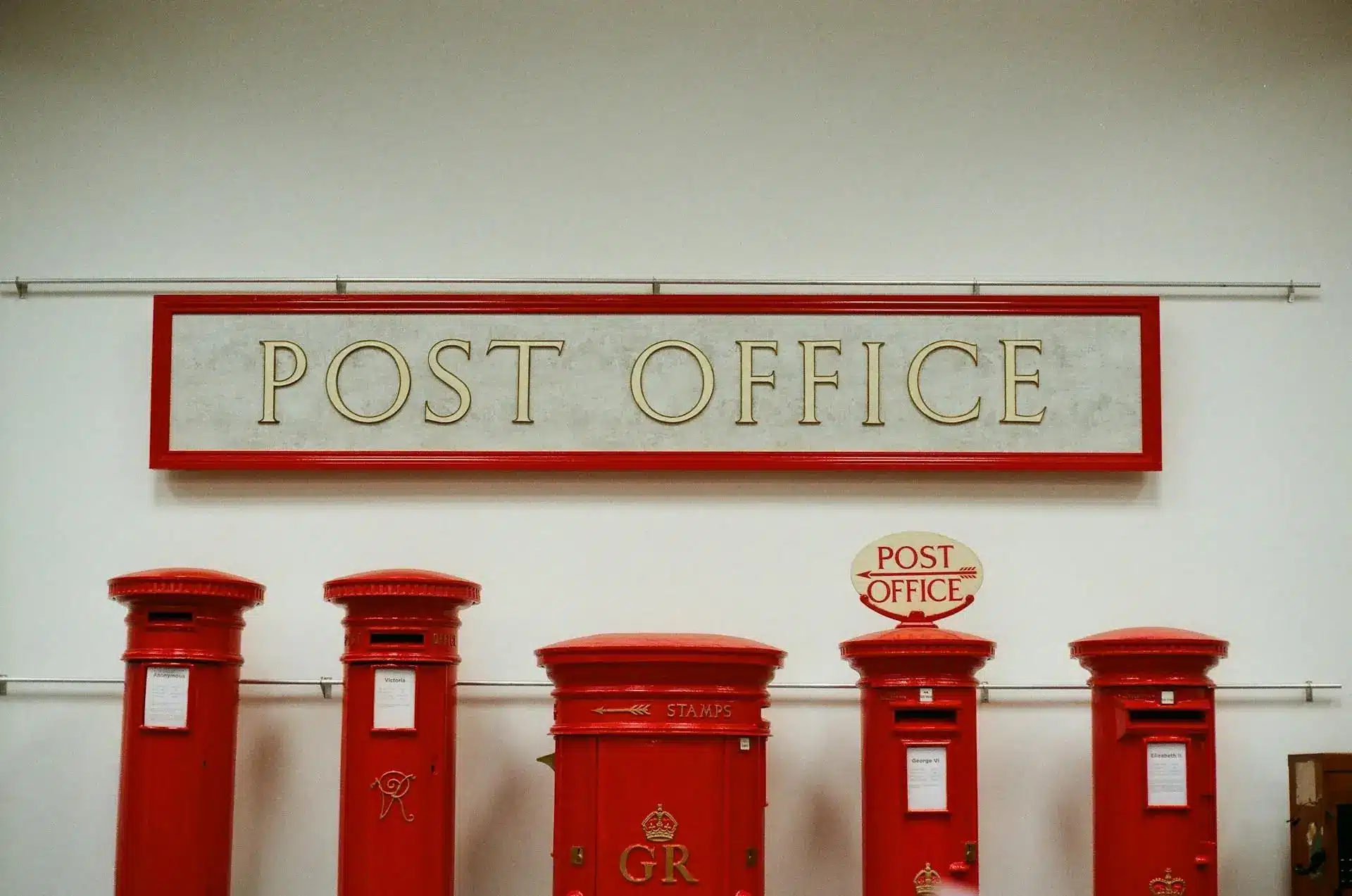 Red vintage post boxes displayed under a large post office sign indoors