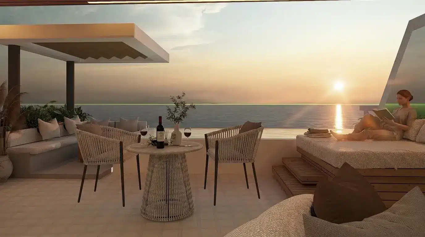 Outdoor terrace with wicker chairs, table with wine, person reading by ocean at sunset