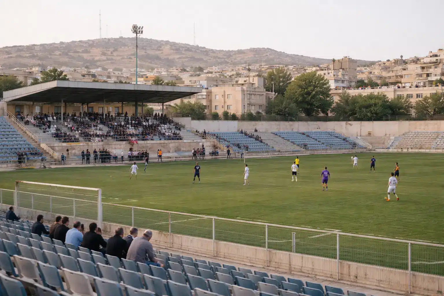Soccer match in a stadium with few spectators and urban backdrop