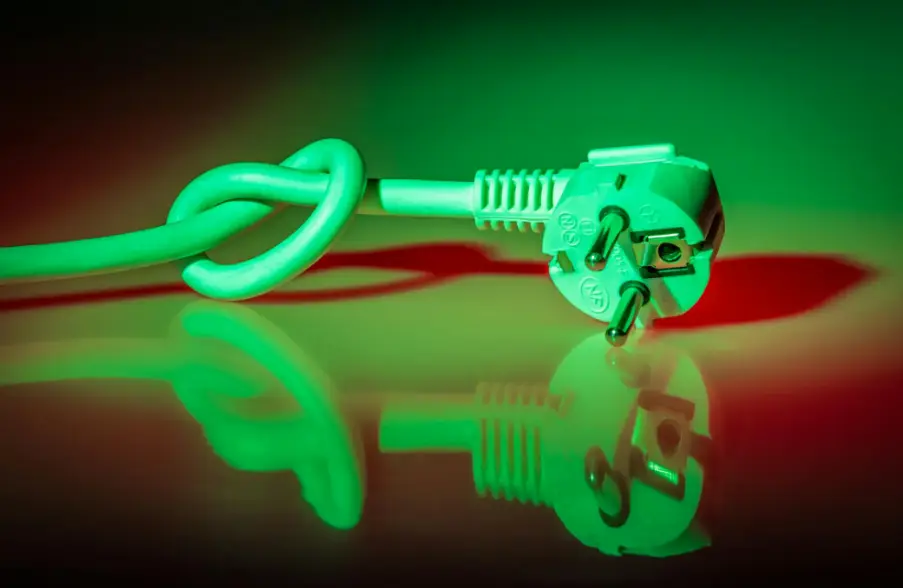 European electrical plug with knotted cord under green and red lighting on reflective surface