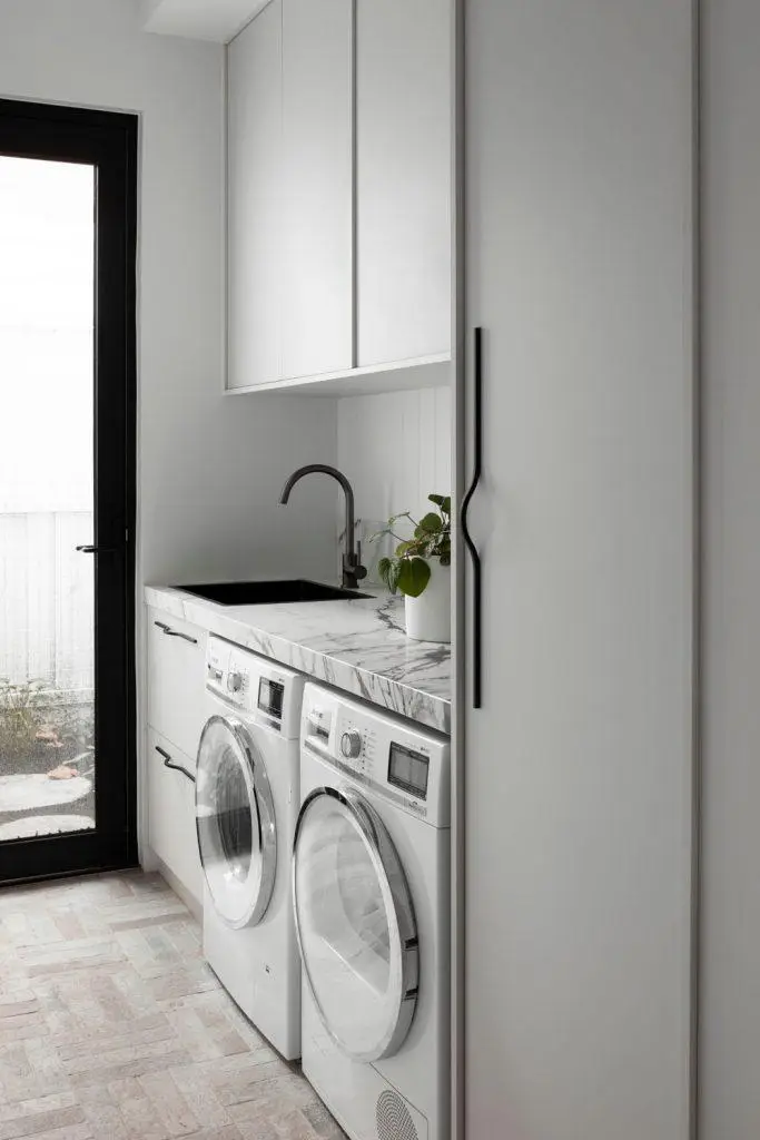 Modern laundry room with front-loading washer and dryer, marble countertop, and potted plant on top