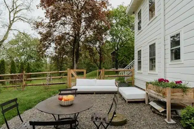 Backyard patio with white outdoor furniture, round table, and wooden planters under overcast sky