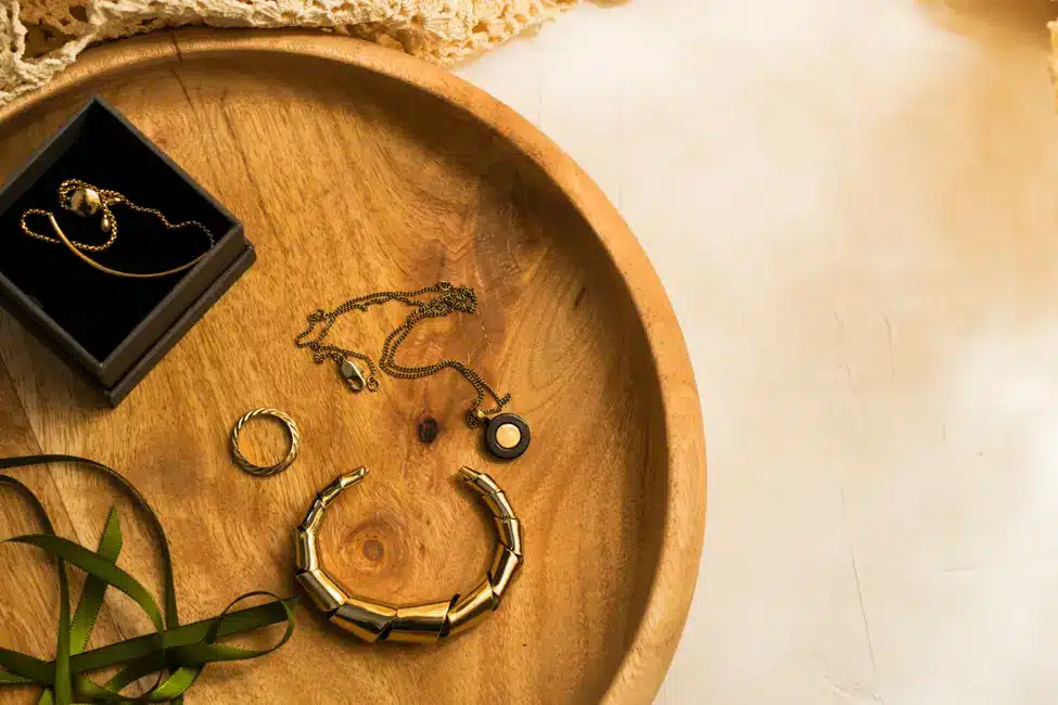 Gold jewelry set with necklace, ring, and bracelet on wooden plate in warm lighting