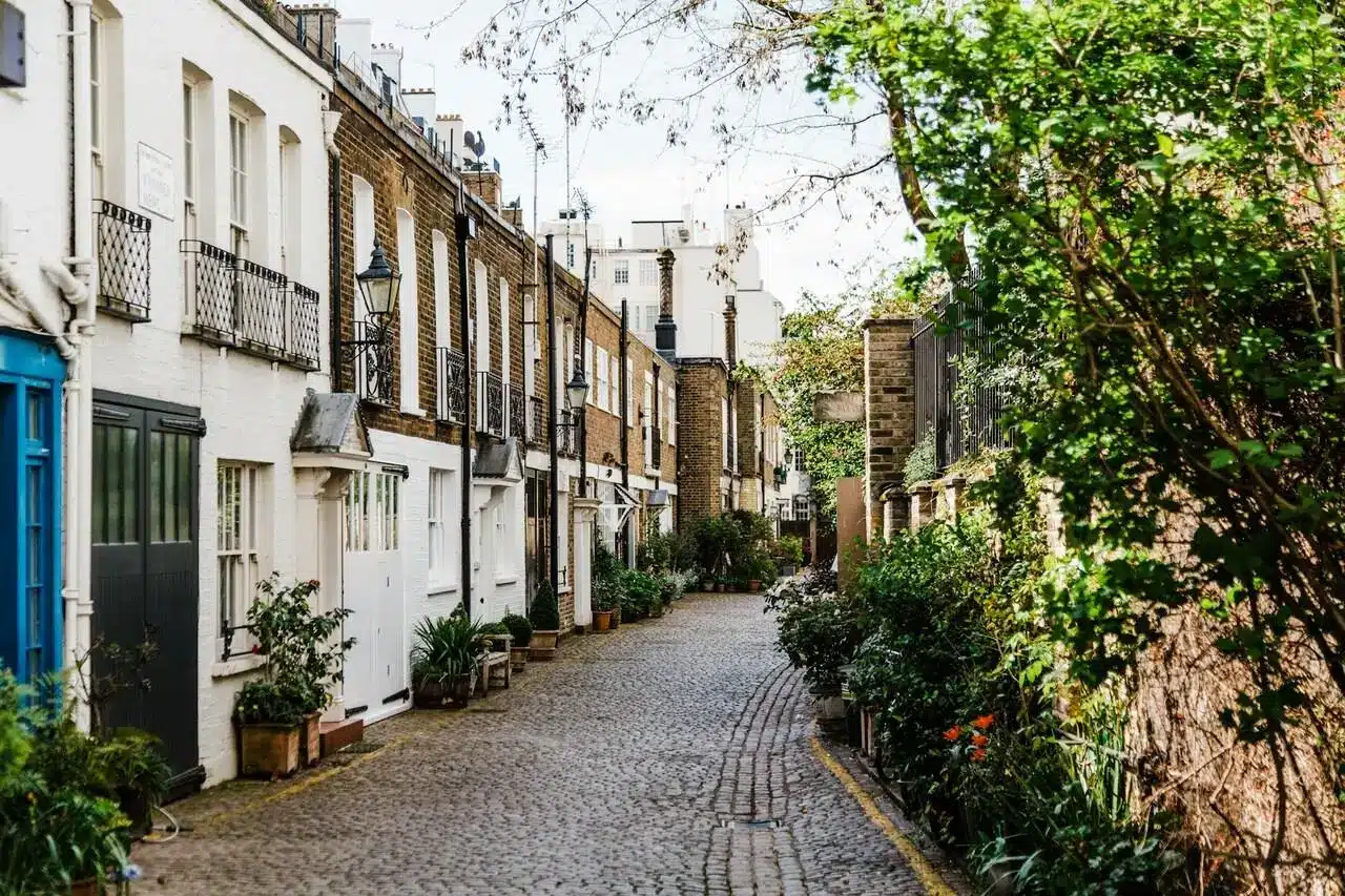 Charming cobblestone street lined with brick and white townhouses, vibrant green foliage