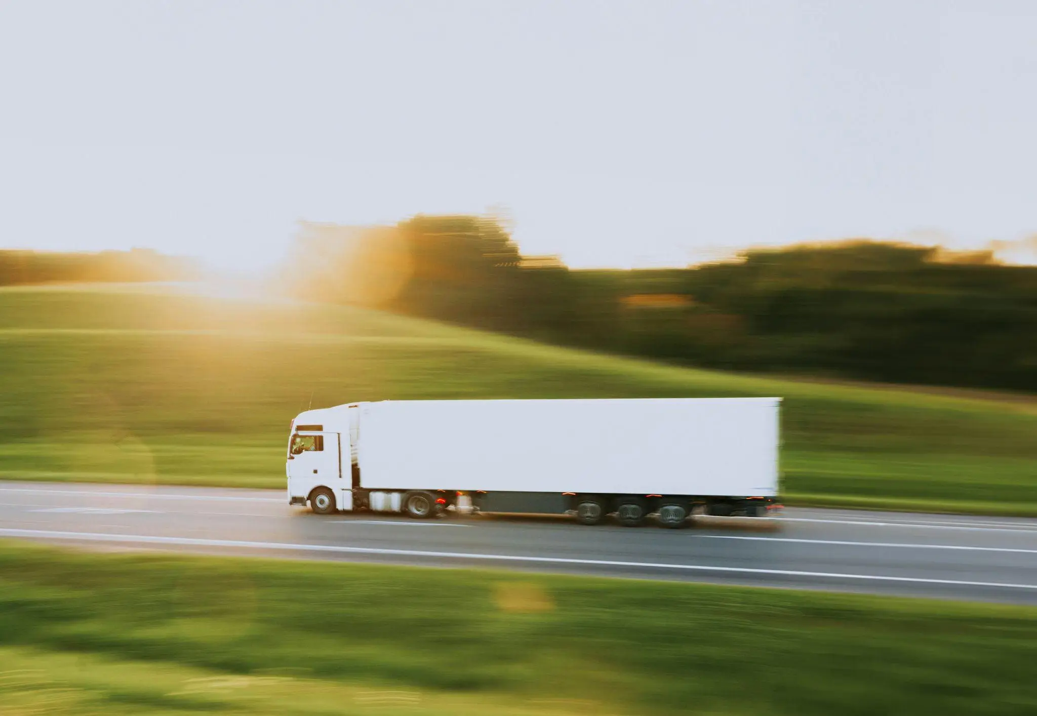 White truck driving on highway through grassy landscape during golden hour