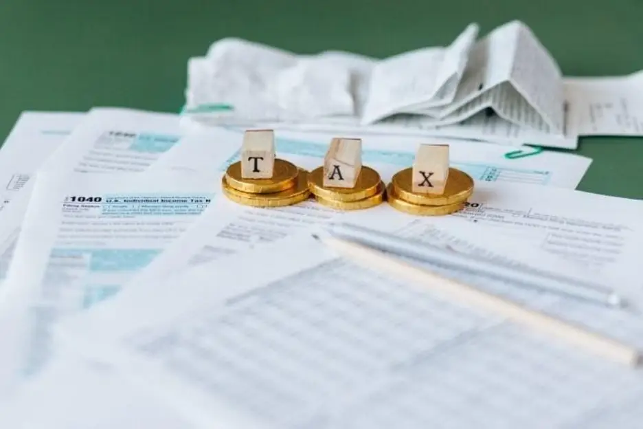 Tax documents and receipts on table with gold coins spelling "TAX"