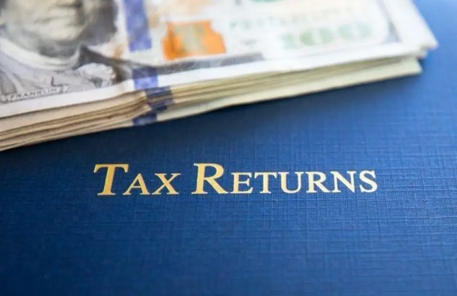 Stack of hundred-dollar bills on blue tax returns document