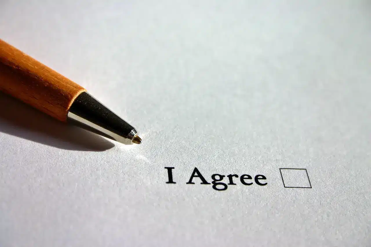 Pen resting on paper with "I Agree" and an unchecked box
