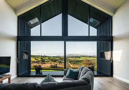 Spacious living room with large glass windows overlooking scenic countryside view and gray sectional sofa