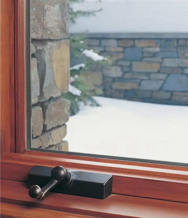 Wooden window frame with bronze handle overlooking snowy garden and stone wall