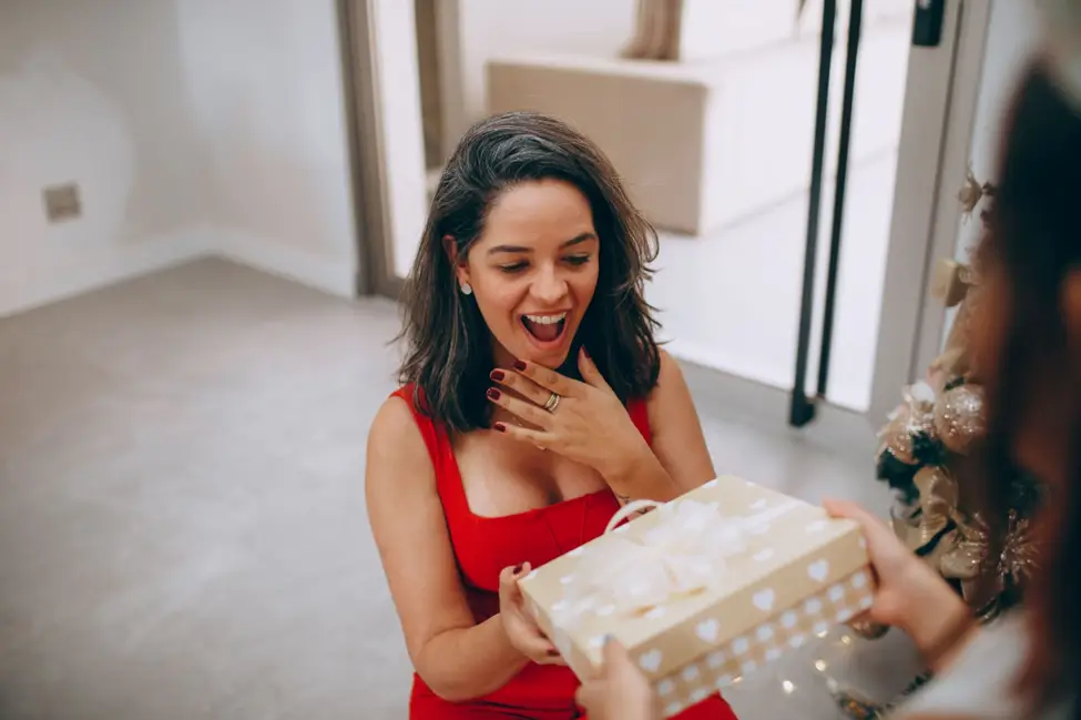 Woman in red dress joyfully receiving a gift in decorated indoor setting