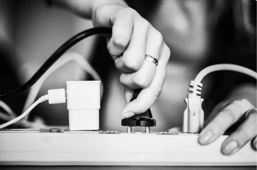 Hand plugging black electric cord into power strip in monochrome setting