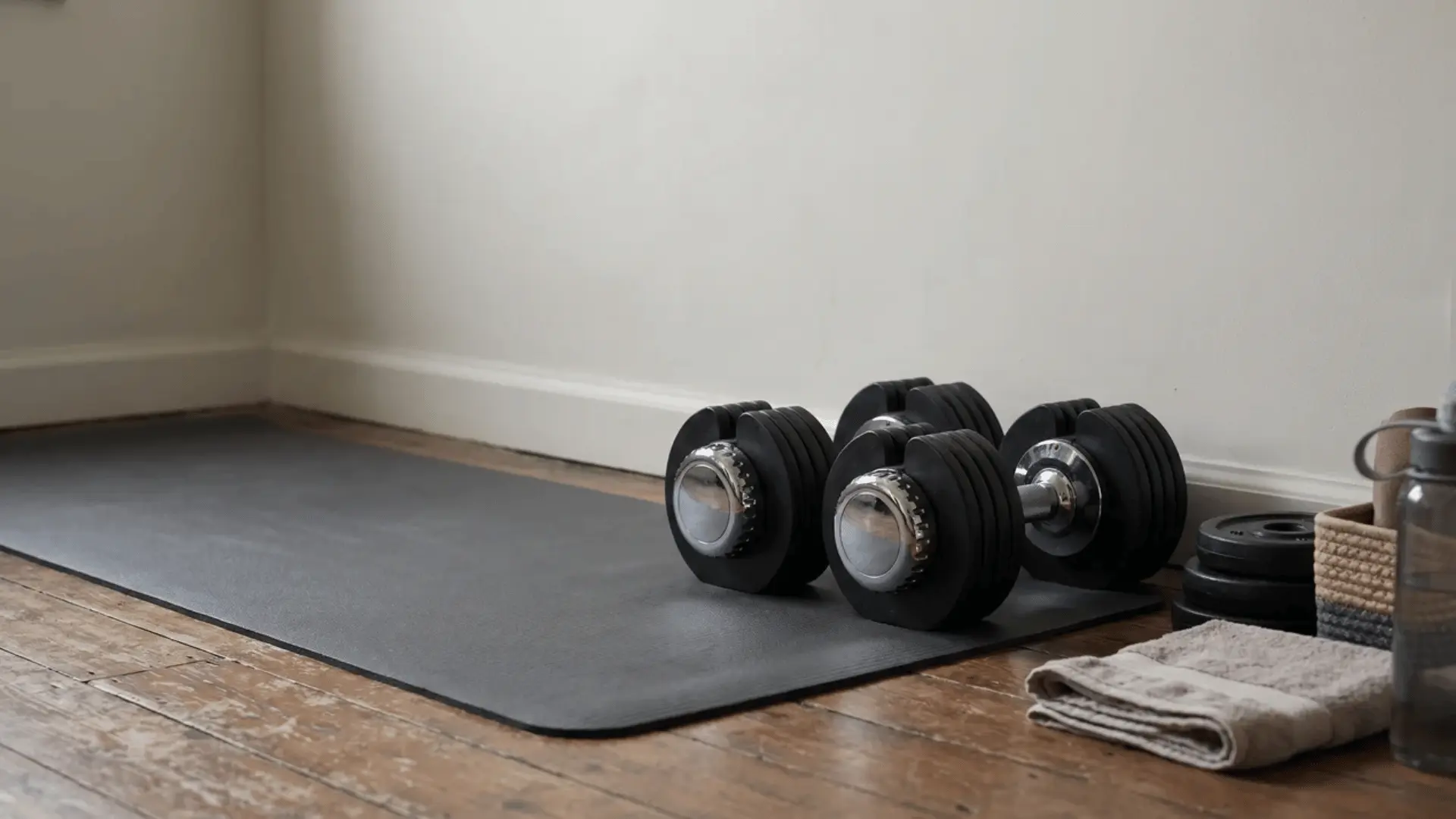 Adjustable dumbbells stored beside a workout mat in a small home workout area