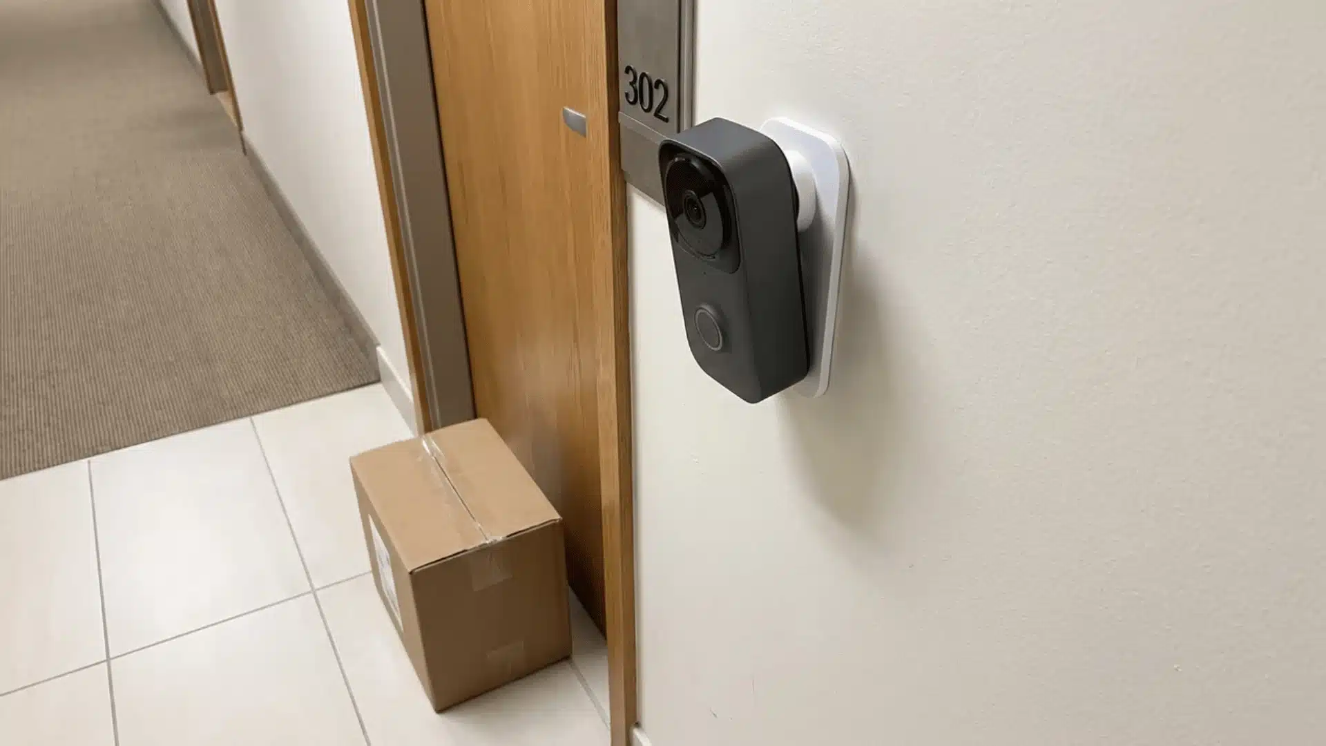 Battery doorbell camera on an adhesive apartment-door mount with a package below