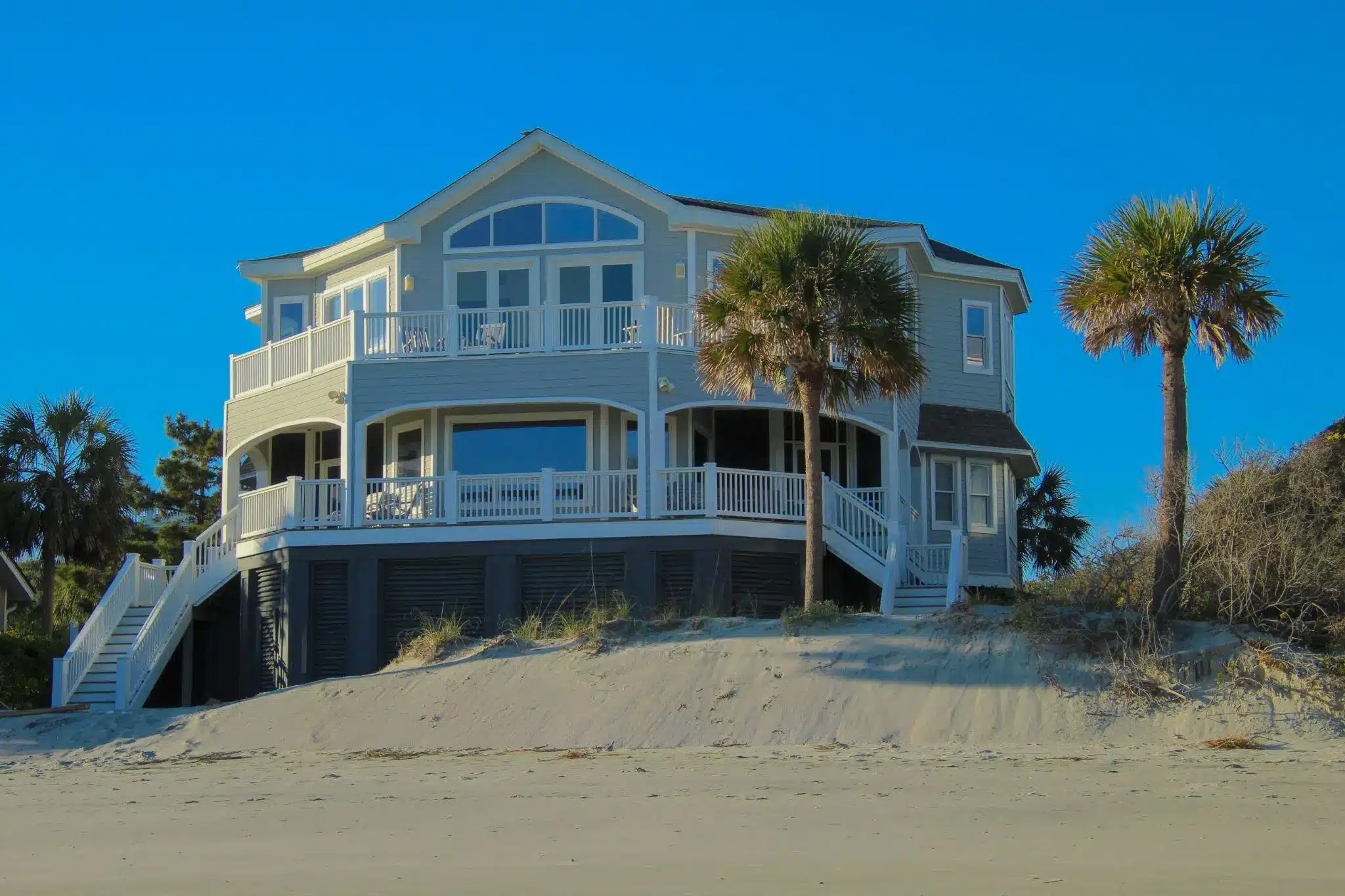 Beachfront house with white railings and palm trees, set against a clear blue sky