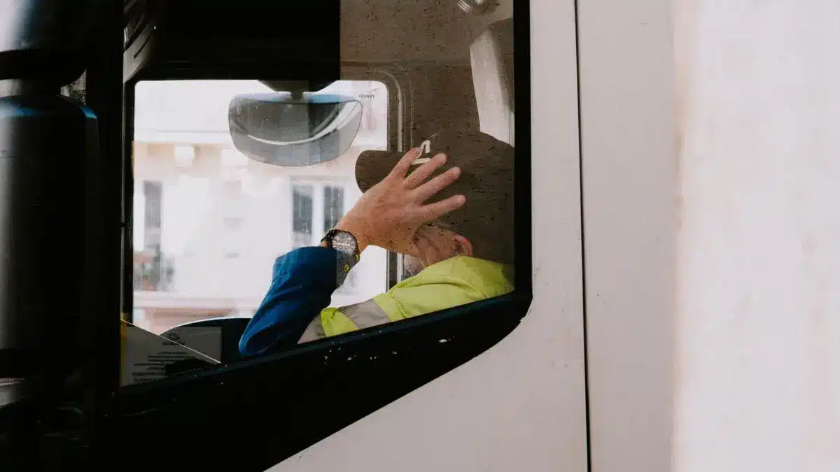 Truck driver wearing a cap inside the cab seen through window in daylight