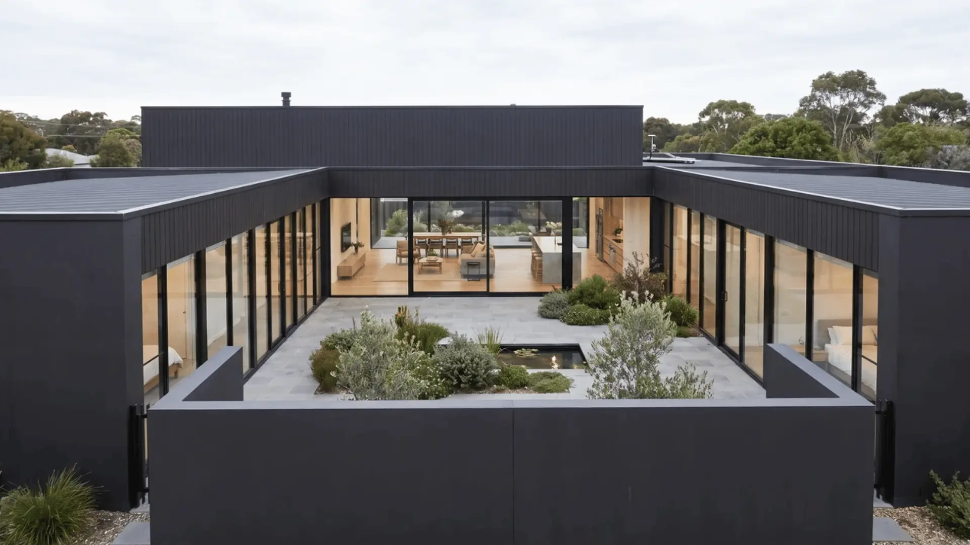 Black modern house surrounding a central courtyard with solid outer walls and interior glass panels