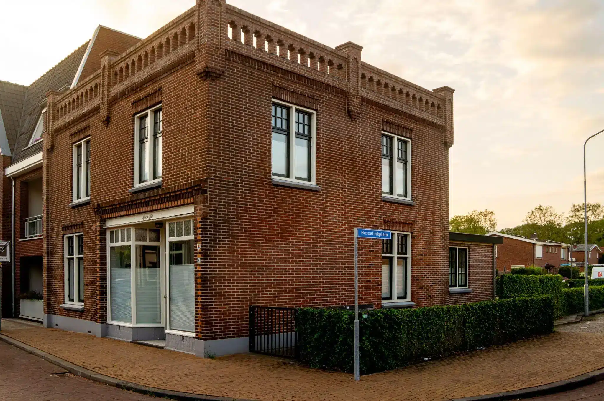 Brick corner building with large windows and hedge on a quiet residential street in evening light